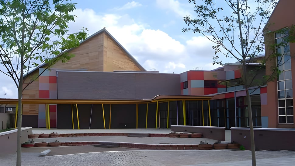 El moderno edificio con techo triangular en el campus de la Townley Grammar School está rodeado de árboles y un área pavimentada.