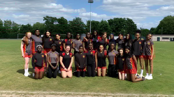 Un grupo de estudiantes de la Townley Grammar School posan juntos en un campo deportivo con un estadio de fondo.