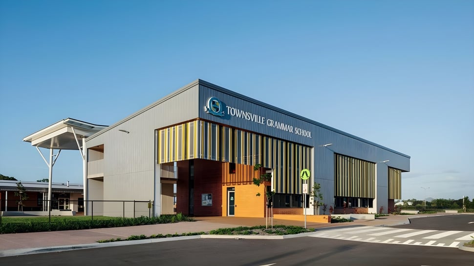 El moderno edificio escolar de la Townsville Grammar School con gran logo y estacionamiento en el frente bajo un cielo despejado.