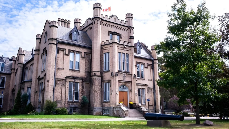 El histórico edificio de ladrillo con torres de la Trafalgar Castle School se encuentra en un patio bordeado de árboles con un cañón en primer plano.