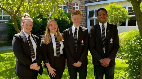 Cuatro estudiantes en uniformes escolares están juntos en el campus de la Trafalgar School al aire libre.