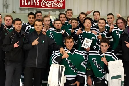 Un grupo de estudiantes en uniformes deportivos verdes y blancos posa frente a un cartel rojo de Coca-Cola en el terreno de la Transcona Collegiate.