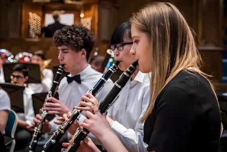 Un grupo de jóvenes músicos toca instrumentos de viento en el Trent College frente a un fondo de madera.