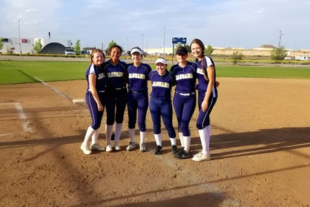 Un grupo de jugadoras de softball está en el campo de la Tri-Cities Prep Catholic High School.