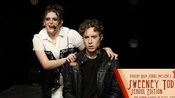 Una mujer y un hombre están de pie frente a un letrero con la inscripción Trident High School.