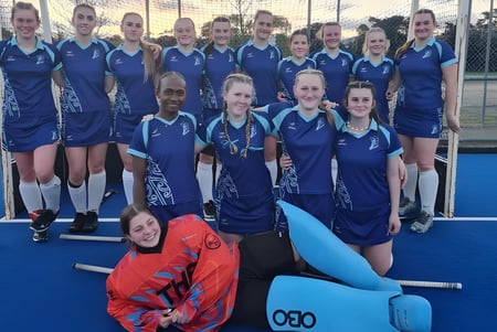 Un grupo de jóvenes atletas en uniformes azules posan en el campo de deportes de la Trident High School frente a un gran objeto inflable.