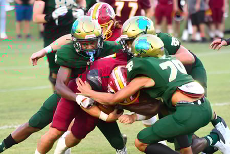Estudiantes de la Trinity Catholic High School realizan una intensa escena de tackle de fútbol americano en el campo.