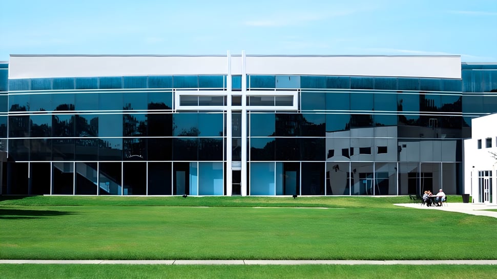 El moderno edificio de la Trinity Christian Academy con fachada de vidrio se encuentra frente a un césped verde bajo un cielo azul.