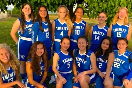 Un grupo de jóvenes estudiantes en uniformes deportivos azules posan juntos al aire libre en el terreno de la Trinity Christian School.