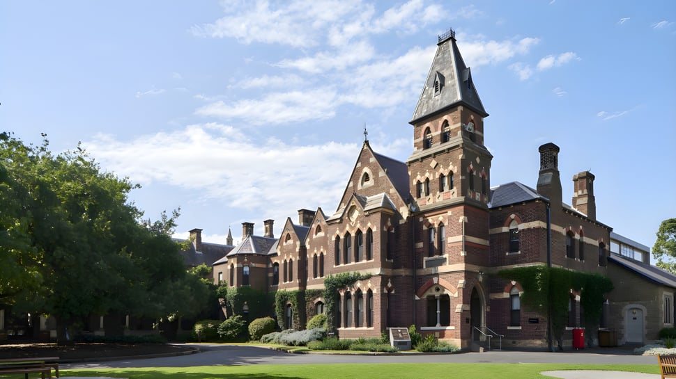El histórico edificio de ladrillo con alto torre en el campus del Trinity College está rodeado de árboles verdes.