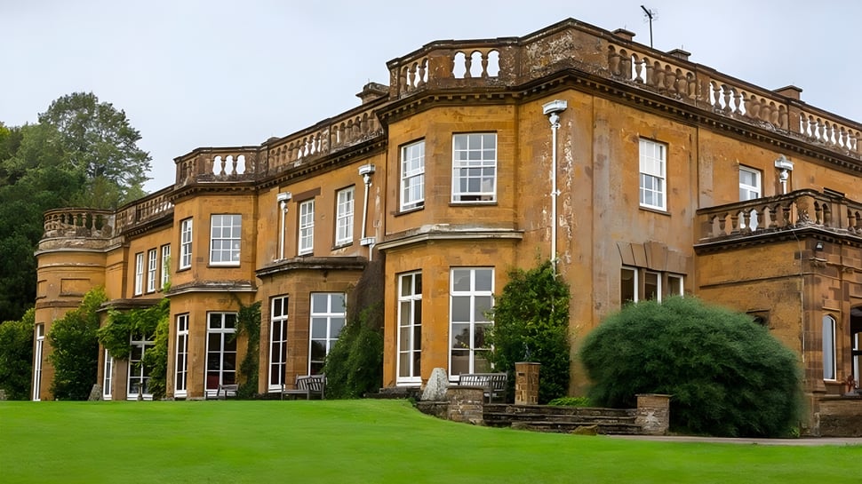 El histórico edificio de ladrillo de Tudor Hall School con arcos y balcones se encuentra frente a un césped verde.