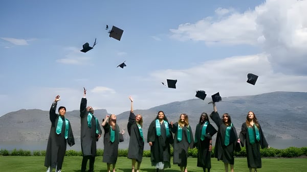 Un grupo de graduados de la Unisus School lanza sus birretes al aire frente a un lago y montañas.