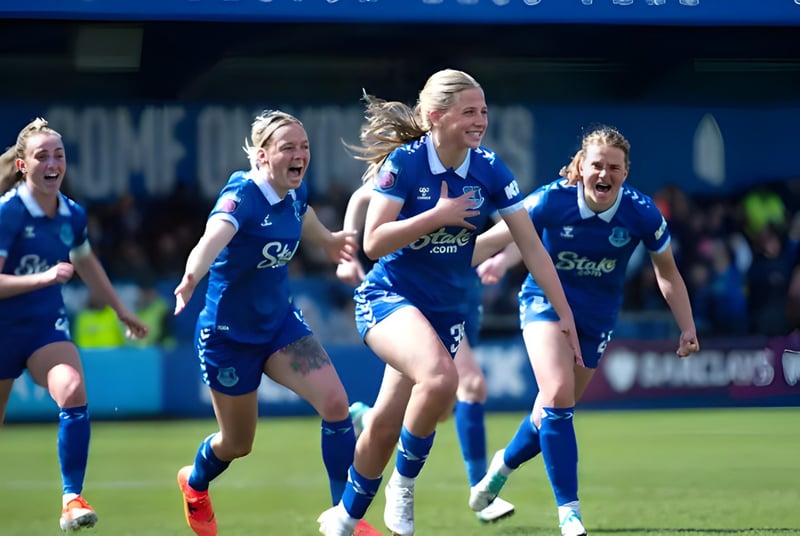 Un grupo de jugadoras de fútbol de la Unisus School corre juntas en el campo frente a un estadio.