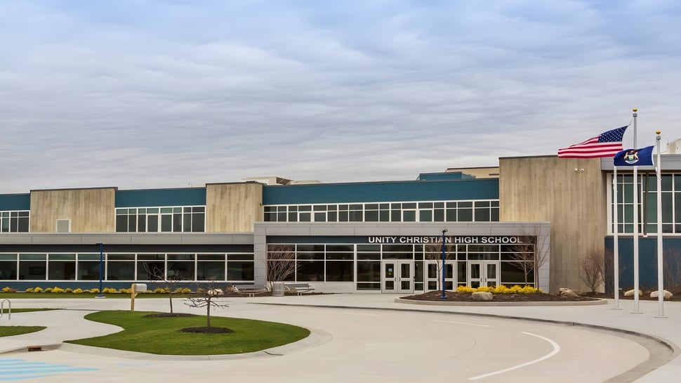 Se puede ver el moderno edificio escolar de la Unity Christian High School con la bandera americana y caminos pavimentados.