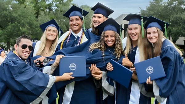 Un grupo de graduados de la University of North Florida está afuera con togas y birretes azules rodeados de árboles.