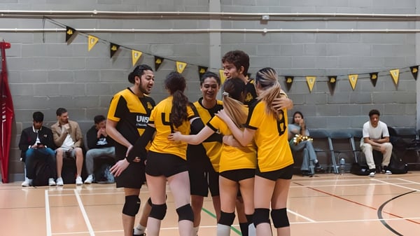 Un grupo de estudiantes de la University of Westminster celebra juntos en un gimnasio con cancha de baloncesto.
