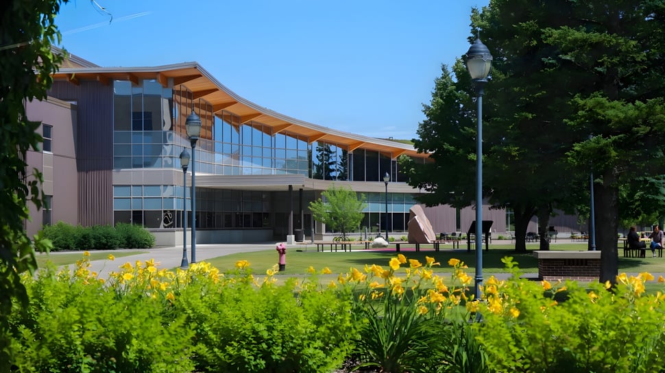 Edificio de la University of Wisconsin-Superior con fachada de vidrio y techo curvado en un paisaje verde con flores amarillas.