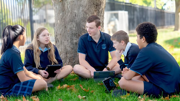 Un grupo de estudiantes de la Unley High School está sentado bajo un árbol y utiliza dispositivos electrónicos para el aprendizaje colaborativo.