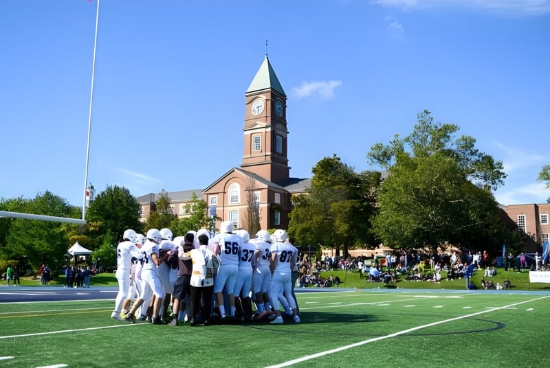 Un grupo de estudiantes en uniformes blancos está de pie sobre un campo en el terreno del Upper Canada College frente a un alto campanario.