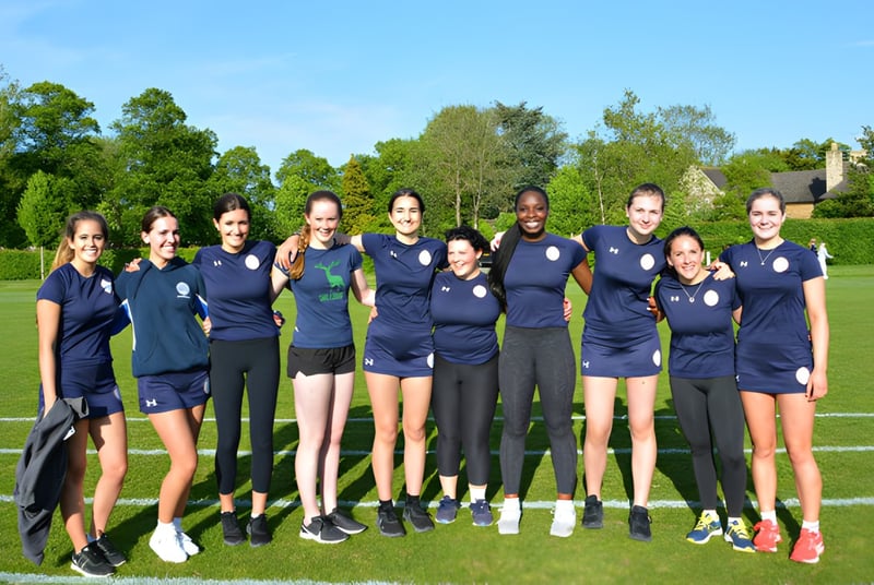 Un grupo de jóvenes atletas de la Uppingham School está reunido en un campo bajo un cielo azul.