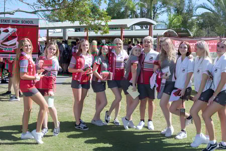 Un grupo de jóvenes alumnas está en uniformes deportivos frente al edificio de la Urangan State High School.