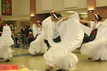Estudiantes del Urbandale Community School District realizan un baile tradicional con trajes blancos y tocados en un espacio interior público.