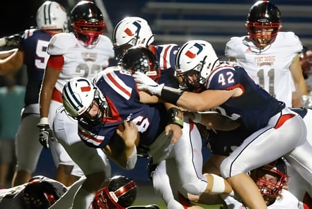 Estudiantes de Urbandale High School realizan un tackle de fútbol americano en el campo.