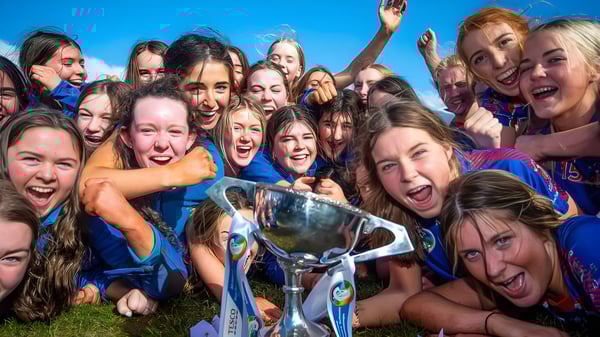 Un grupo de jóvenes estudiantes de la Ursuline Secondary School Thurles está afuera juntas y sostiene un trofeo en la mano.