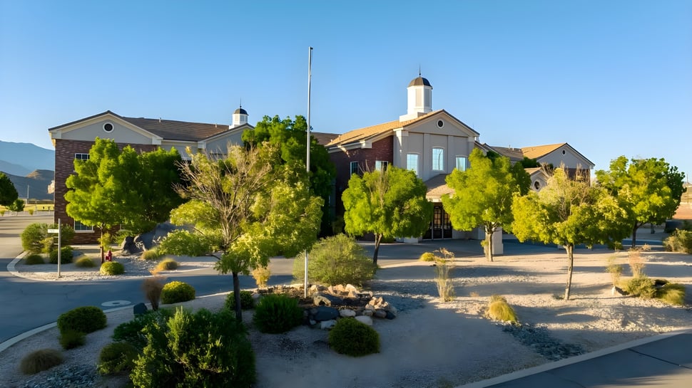 Zona verde con arbustos y árboles bien cuidados en el campus de la Utah Prep Academy bajo un cielo despejado.