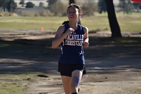 Una estudiante de la Vacaville Christian School corre por un sendero forestal rodeada de árboles y vegetación.