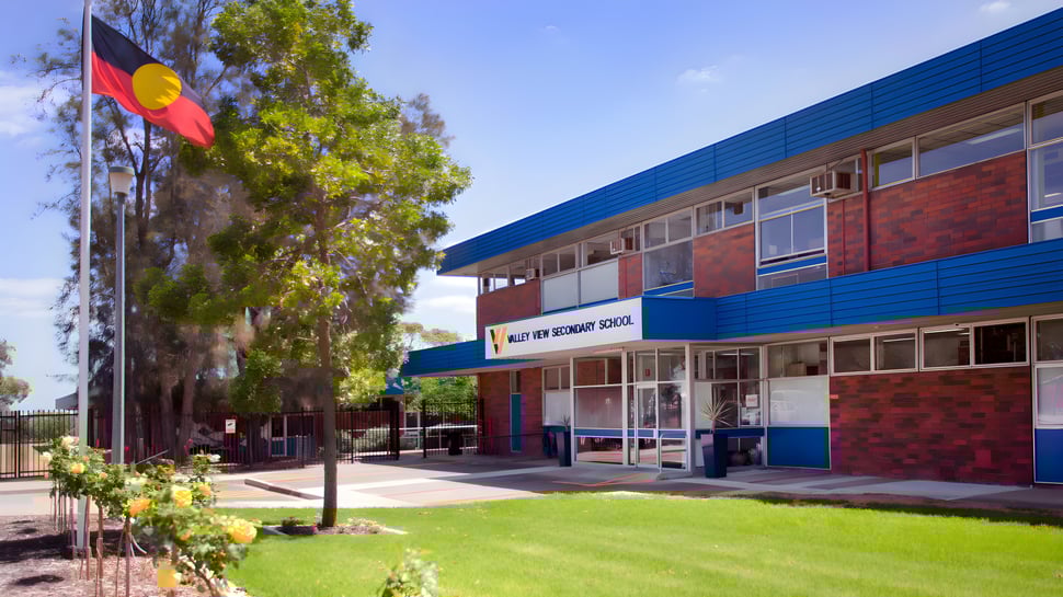 El moderno edificio de varios pisos de la Valley View Secondary se encuentra en un prado y está rodeado de árboles.