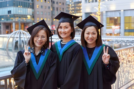 Tres graduadas del Vancouver Community College están frente al horizonte de una ciudad moderna.