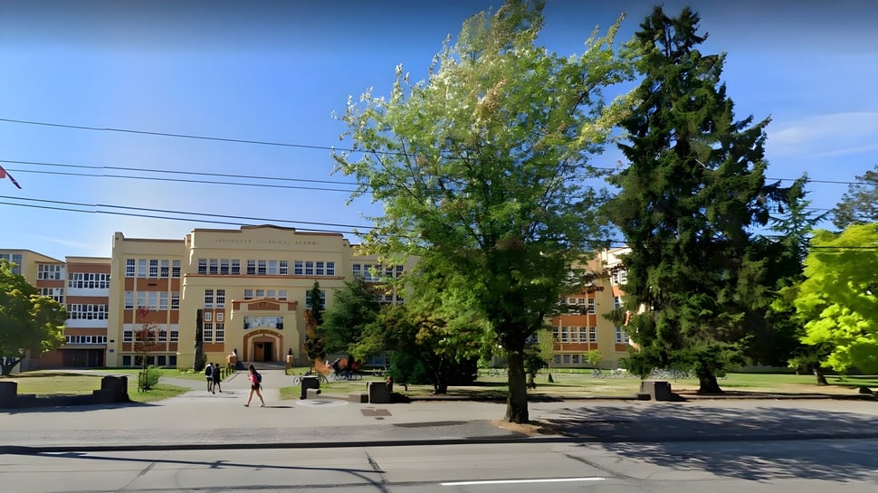 El campus de Vancouver Technical Secondary School muestra grandes árboles frente a edificios escolares de varios pisos bajo un cielo despejado.