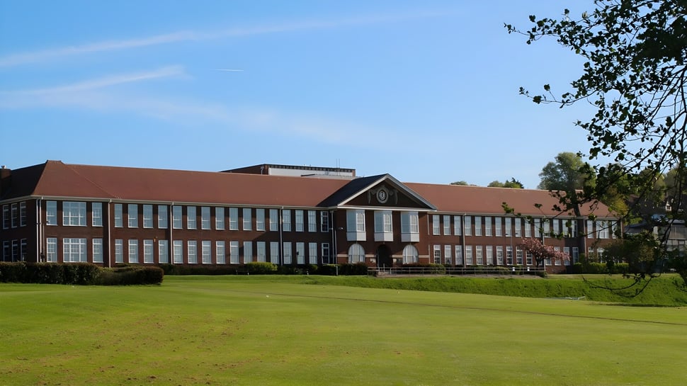 El edificio de ladrillo de varios pisos con techo rojo en el campo verde del Varndean College.