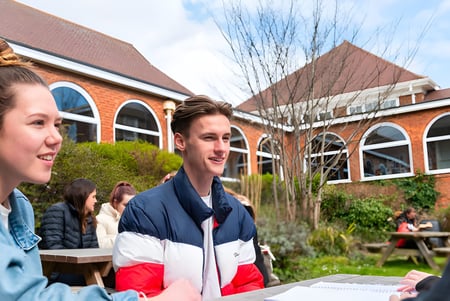 Estudiantes conversan en un día soleado frente a un edificio de ladrillo en el campus del Varndean College.