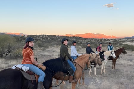 Estudiantes de la Verde Valley School montan a caballo a través de un paisaje desértico pintoresco con montañas al fondo.