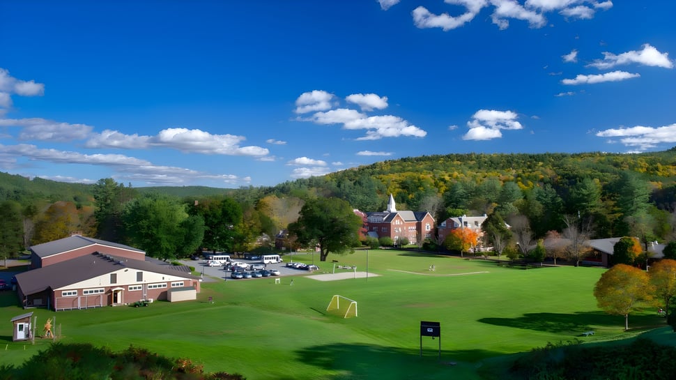 Un campo de golf verde con hojas de otoño de colores y un pueblo con un campanario de fondo en el campus de la Vermont Academy.