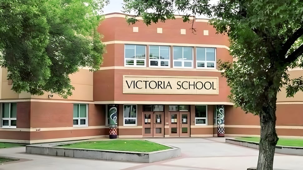 El edificio de ladrillo de la Victoria School of the Arts está rodeado de árboles verdes y una superficie de césped.