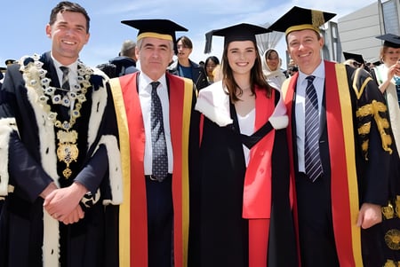 Un grupo de estudiantes de la Victoria University of Wellington en togas de graduación posa frente a un edificio universitario.