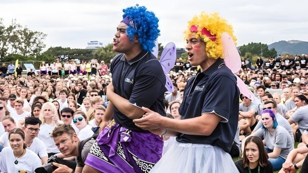 Dos personas con cabello colorido están frente a una gran multitud en el campus de la Victoria University of Wellington.