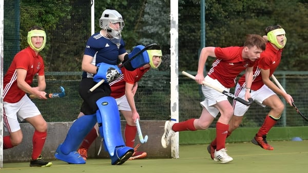 Estudiantes de la Villiers School juegan un partido de hockey en un campo con árboles de fondo.
