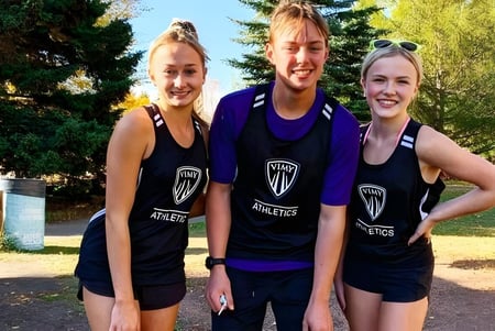 Tres estudiantes de la Vimy Ridge Academy están juntos al aire libre en uniformes deportivos de equipo frente a un fondo parecido a un parque.