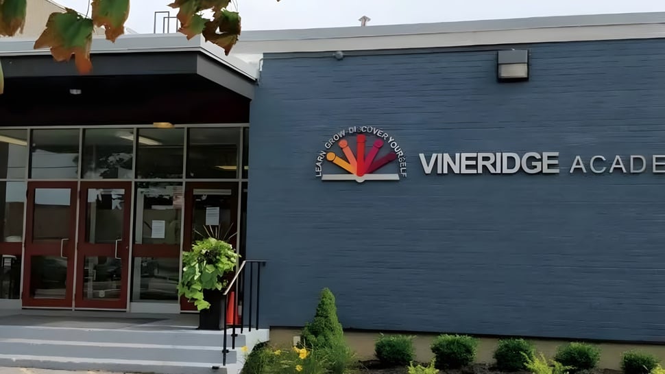 El edificio de la Vineridge Academy con el letrero afuera y el camino hacia la entrada está rodeado de pequeñas plantas.