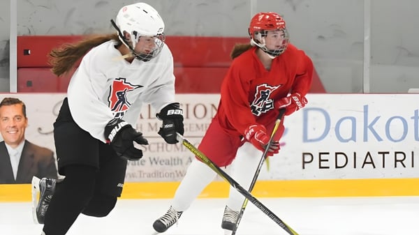 Dos jugadores de hockey de la Vineridge Academy en camisetas blancas y rojas juegan en el campo de hielo.