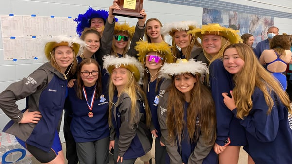 Un grupo de alumnas del Virginia Beach City Public School District posa con pelucas coloridas y disfraces frente a carteles escolares.