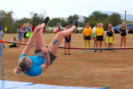 Una estudiante realiza un ejercicio de gimnasia sobre una colchoneta en el área exterior del Waihi College frente a un grupo de espectadores.