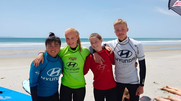 Un grupo de cuatro estudiantes está en la playa con el océano de fondo en el terreno del Waihi College.