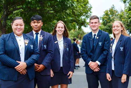 Un grupo de alumnas y alumnos en uniforme se encuentra juntos en el área verde del campus de Waitakere College.