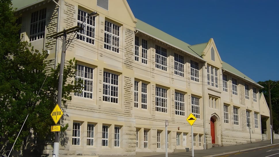 El edificio de ladrillo de varios pisos con grandes ventanas y puerta roja se encuentra en el terreno de la Waitaki Girls’ High School.