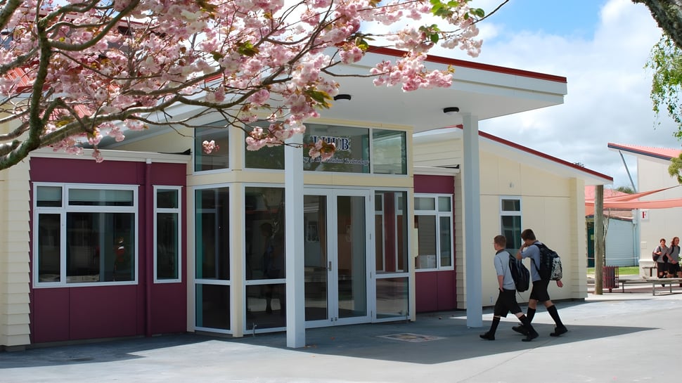Un edificio moderno con entrada de vidrio y un cerezo en flor en primer plano en el campus del Waiuku College.